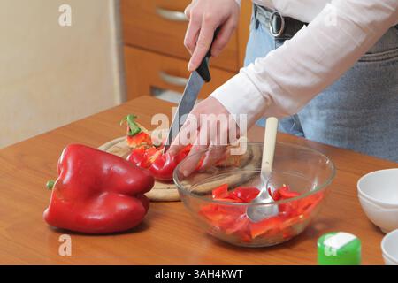 Femme tranchant les poivrons rouges pour une préparation saine des repas dans la cuisine domestique Banque D'Images