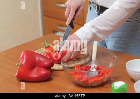Femme tranchant les poivrons rouges pour une préparation saine des repas dans la cuisine domestique Banque D'Images