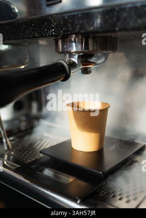 La machine à espresso verse le café dans un gobelet en papier placé sur une balance, créant de la vapeur. Banque D'Images