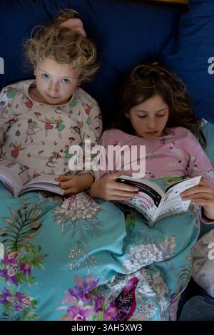Deux enfants sœurs lisant chacune des livres au lit côte à côte. Les filles sont 7 (à gauche) et 9. Banque D'Images