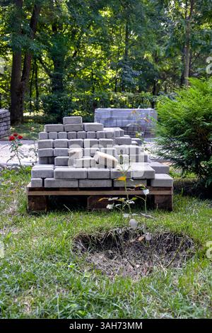 Les dalles de pavage grises préparées pour la pose sont empilées dans une palette en bois près de l'allée du parc le jour ensoleillé d'été. Gros plan. Copier l'espace pour le texte. Banque D'Images