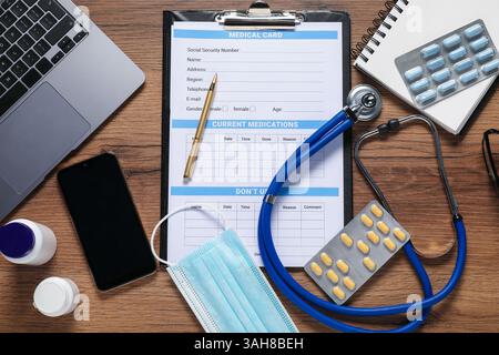 Composition à plat avec forme de carte médicale, smartphone, ordinateur portable, pilules et stéthoscope sur table en bois Banque D'Images