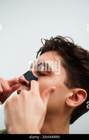 Homme avec bande de nez de charbon de bois pour le nettoyage des pores. Jeune homme appliquant une bande de nez de charbon de bois pour le nettoyage profond des pores du nez. Concept de beauté masculine et de soins de la peau Banque D'Images