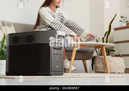 Centrale électrique portable contre la femme assise sur le canapé à la maison, gros plan Banque D'Images