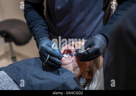 Dentiste portant des gants noirs examinant les dents d'une femme âgée allongée dans un fauteuil dentiste lors d'un bilan de santé Banque D'Images