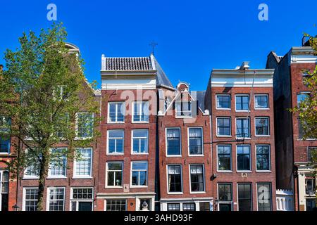 Maisons étroites inclinées tordues le long d'un canal à Amsterdam. Maisons dansantes d'Amsterdam gros plan contre le ciel bleu. Bâtiments historiques médiévaux en th Banque D'Images