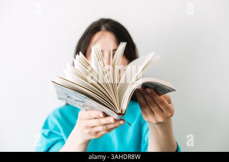 Une jeune femme tient un journal ouvert avec des pages flottantes devant son visage. Auto-réflexion, journalisation comme thérapie, routines conscientes, analogique Banque D'Images