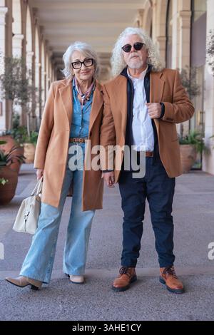 Portrait vertical d'un couple senior souriant marchant à l'extérieur dans des vestes élégantes Banque D'Images