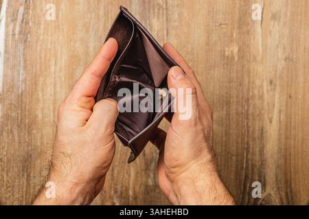 Un homme tient son portefeuille vide, visiblement affligé par sa situation financière. Ce moment reflète le désespoir et l'impact des défis économiques. Banque D'Images
