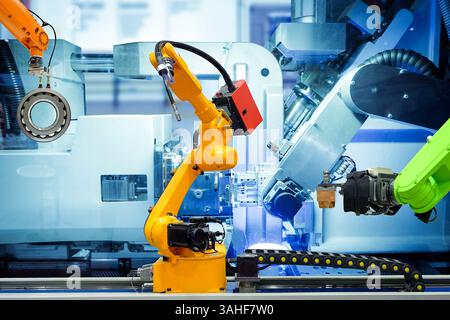 Robot industriel de soudage et robot de préhension travaillant avec des pièces métalliques sur usine intelligente, sur fond de couleur bleu machine, industrie 4,0 Banque D'Images