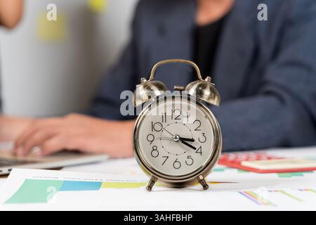 Homme d'affaires reposant la tête sur le bureau. Gros plan du réveil sur le bureau avec ordinateur portable. Freelance travaillant dans un ordinateur portable avec réveil à côté. Réveil sur le Banque D'Images