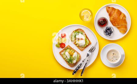 Petit déjeuner avec de délicieux toasts à l'avocat garni d'œufs pochés parfaitement cuits et croissant croustillant avec des baies et de la confiture Banque D'Images