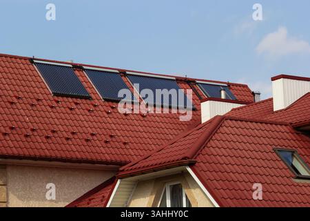 Les panneaux solaires sont montés sur les toits de tuiles rouges des maisons dans un cadre de banlieue sous un ciel bleu clair, mettant en valeur l'intégration des énergies renouvelables dans la résidence Banque D'Images
