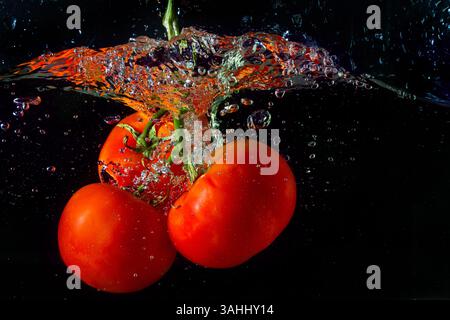 Tomate rouge fraîche tombant dans l'eau avec des éclaboussures d'eau et des bulles d'air isolées sur fond noir. Banque D'Images