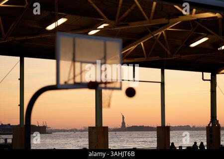 Silhouette de basket-ball et de ballon contre un coucher de soleil avec la Statue de la liberté au loin. New York, États-Unis Banque D'Images