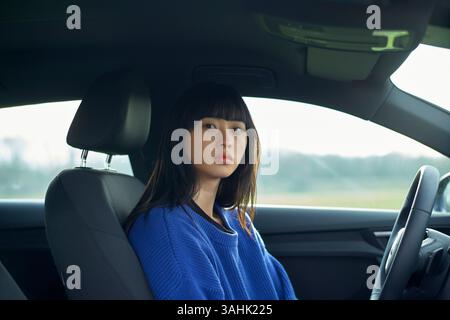 Une femme en pull bleu est assise sur le siège du conducteur d'une voiture, regardant directement devant. Brandebourg, Allemagne Banque D'Images