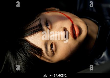 Femme allongée avec une traînée rouge sur son visage, portant une tenue sombre. Brandebourg, Allemagne Banque D'Images