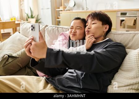 Couple profitant d'un moment léger tout en prenant un selfie sur le canapé à la maison. Banque D'Images
