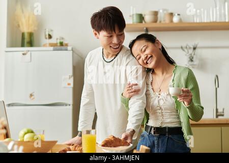 Un jeune couple partage le rire tout en dégustant le petit déjeuner ensemble dans leur cuisine confortable. Banque D'Images