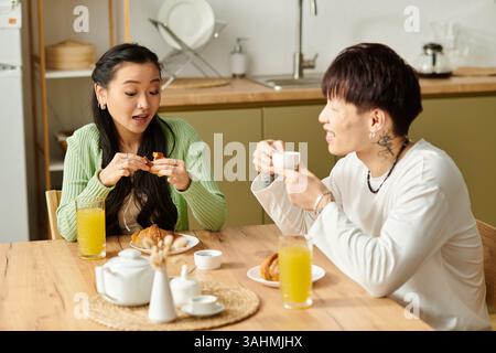 Un jeune couple asiatique profite d'un délicieux petit déjeuner ensemble à la maison, riant et partageant la nourriture. Banque D'Images