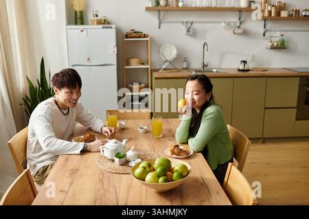Un jeune couple profite d'un délicieux petit déjeuner à la maison, rempli de rires et de fruits frais. Banque D'Images
