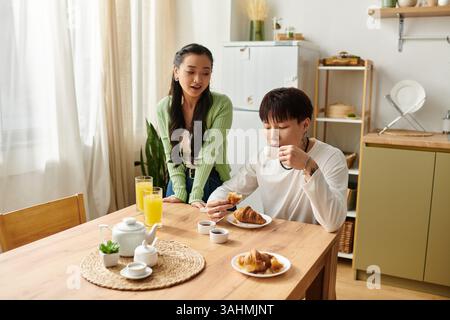 Un jeune couple profite d'un délicieux petit déjeuner ensemble, en savourant des pâtisseries et des boissons dans leur maison. Banque D'Images