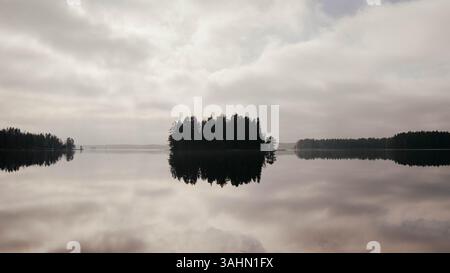 Un lac serein en Suède, avec une île entourée d'arbres luxuriants, avec un reflet époustouflant sur l'eau calme. La scène paisible et tranquille c Banque D'Images