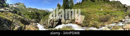 Une vue imprenable à grand angle avec un ruisseau alpin qui coule sur fond de montagnes verdoyantes et de ciels bleus, mettant en valeur la beauté naturelle Banque D'Images
