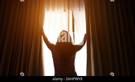 Femme ouvrant des rideaux dans la chambre d'hôtel laissant entrer la lumière Banque D'Images