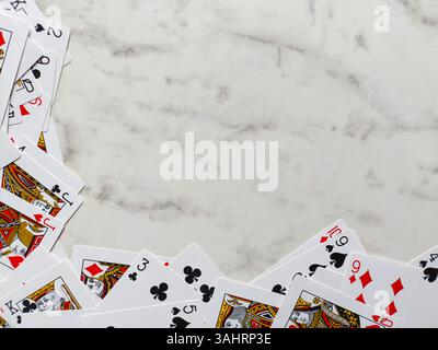 arrangement dispersé de cartes à jouer sur une surface de marbre blanc. Les cartes sont principalement positionnées autour des bords inférieur et gauche du cadre Banque D'Images