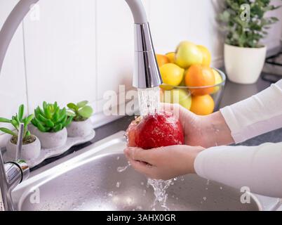 Les mains de la femme lavant la pomme rouge fraîche dans la cuisine. Manger des aliments biologiques crus sains, des vitamines, laver les fruits des pesticides concept. Banque D'Images