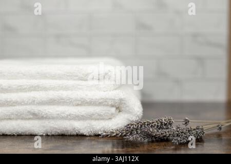 Serviettes éponge blanches dans la salle de bains. Serviettes sur un fond en bois. Fleurs de lavande séchées. Photo de haute qualité Banque D'Images