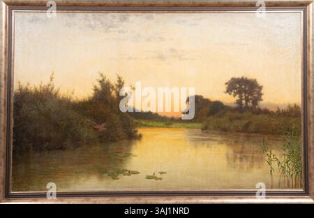 Uferlandschaft mit Seerosen im Abendlicht (paysage riverain avec des nénuphars dans la lumière du soir) d'Eduard Ockel est une peinture à l'huile sur toile, créée avant 1910. Il représente une scène tranquille au bord du lac au crépuscule, avec des nénuphars flottant à la surface, capturés dans une douce lumière du soir. Banque D'Images