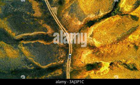 Vue aérienne de la voiture sur terrain accidenté hors route. Vue aérienne d'une voiture naviguant sur un chemin de terre accidenté et sinueux au milieu d'un paysage aride. Banque D'Images