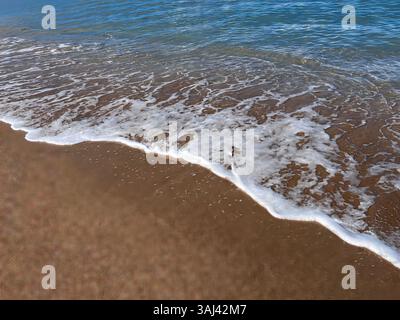De douces vagues de l'océan se jettent sur une plage de sable doré, capturant la beauté sereine de la vie côtière et le rythme apaisant de la nature. Banque D'Images