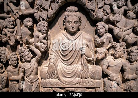 WASHINGTON DC — Un panneau en relief de schiste de l'ancien Gandhara (Pakistan/Afghanistan moderne) représentant les lumières du Bouddha, exposé au Musée national Smithsonian d'art asiatique. Créé sous la dynastie Kushan (fin du IIe siècle - début du IIIe siècle de notre ère), ce panneau faisait partie d'un ensemble de quatre scènes ornant un stupa bouddhiste. La sculpture montre le Bouddha serein en méditation avec sa main dans le geste touchant la terre (bhumisparsha mudra), entouré par l'armée démon déformée de Mara tentant de le distraire de l'accomplissement de l'illumination. Banque D'Images