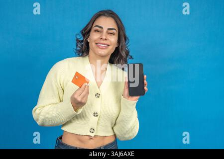 Femme souriante montrant une carte de crédit et un smartphone avec écran vierge, favorisant les achats en ligne et les méthodes de paiement sécurisées Banque D'Images