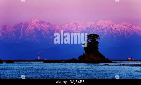 Une vue spectaculaire sur la chaîne de montagnes tsurugitateyama teinte dans le soleil couchant sur la baie de Toyama depuis la plage d'Amaharashi au début du printemps, Takaoka City, Banque D'Images