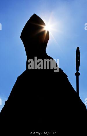 Évêque catholique anonyme avec mitre et crozier comme une silhouette contre la lumière, photo symbolique Banque D'Images