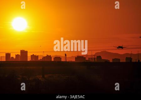 Tempe, Arizona, États-Unis. 10 avril 2025. Un avion de ligne descend vers l'aéroport international Sky Harbor de Phoenix au coucher du soleil, vu du lac de Tempe Town avec la silhouette du centre-ville de Phoenix sur le ciel. Jeudi a marqué le premier jour à trois chiffres de 2025 dans la région de Phoenix, arrivant près d'un mois plus tôt que d'habitude et suivant un record de 2024 avec 70 jours à ou au-dessus de 110 degrés. (Crédit image : © Eduardo Barraza/ZUMA Press Wire) USAGE ÉDITORIAL SEULEMENT ! Non destiné à UN USAGE commercial ! Banque D'Images