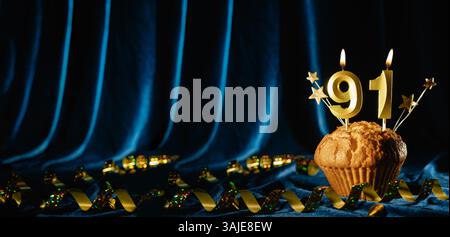 Numéro 91 bougie de célébration en or et petites étoiles dans un cupcake sucré sur fond de velours bleu vif. Concept de célébration d'anniversaire, anniversaire Banque D'Images