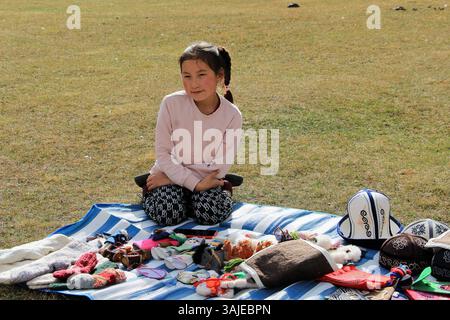 Un enfant kirghize vend des souvenirs traditionnels. La jeune fille vend de l'artisanat comme des chapeaux, des chaussettes, des gants, des jouets. Banque D'Images
