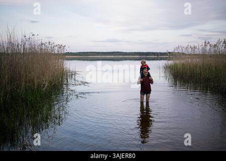 Grand-père portant petit-fils sur les épaules tout en marchant dans le lac Banque D'Images
