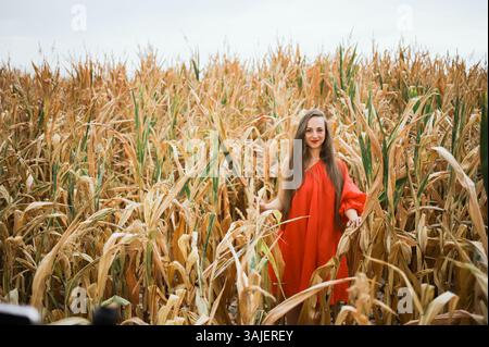 Femme en robe rouge debout dans le champ de maïs en automne Banque D'Images