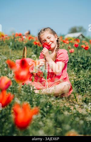Fille sentant la tulipe rouge tout en étant assise dans le champ de printemps coloré Banque D'Images