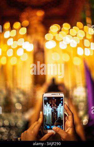 Pendant la semaine Sainte à Séville, une personne photographie le paso de palio de la Vierge de la victoire au milieu d’une procession vibrante remplie de lumières. Banque D'Images