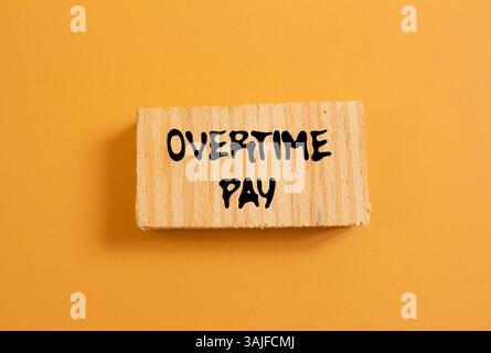 Message de paie d'heures supplémentaires écrit sur morceau de bois sur fond orange. Symbole conceptuel de rémunération des heures supplémentaires. Copier l'espace. Banque D'Images