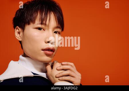 Un beau jeune homme asiatique met en valeur son sens de la mode avec charme, placé contre un mur orange audacieux. Banque D'Images