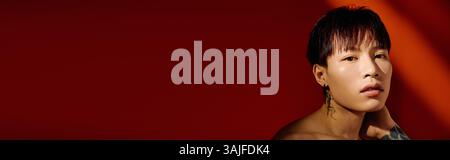 Beau jeune homme respire le charme et le style avec des tatouages, sur un fond rouge vif. Banque D'Images