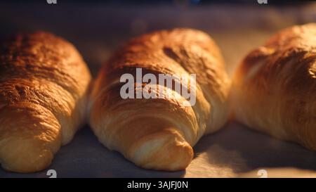 Trois croissants cuits au four sur du papier sulfurisé. Macro-photographie culinaire en gros plan. Processus de cuisson et concept de boulangerie pour la conception et l'impression Banque D'Images